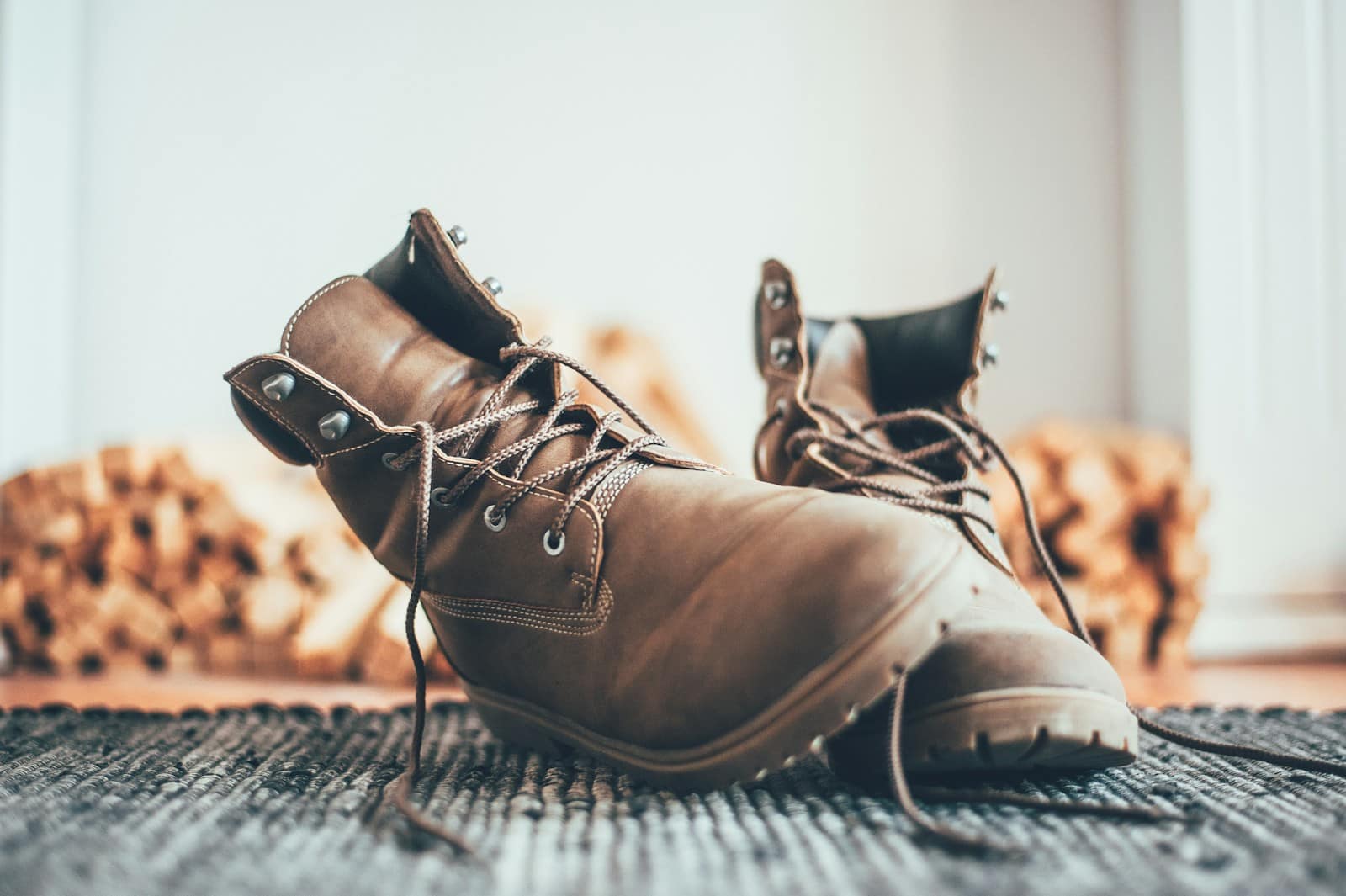 A pair of worn brown leather boots on a woven mat, laces undone, the lugged outsole edge in focus