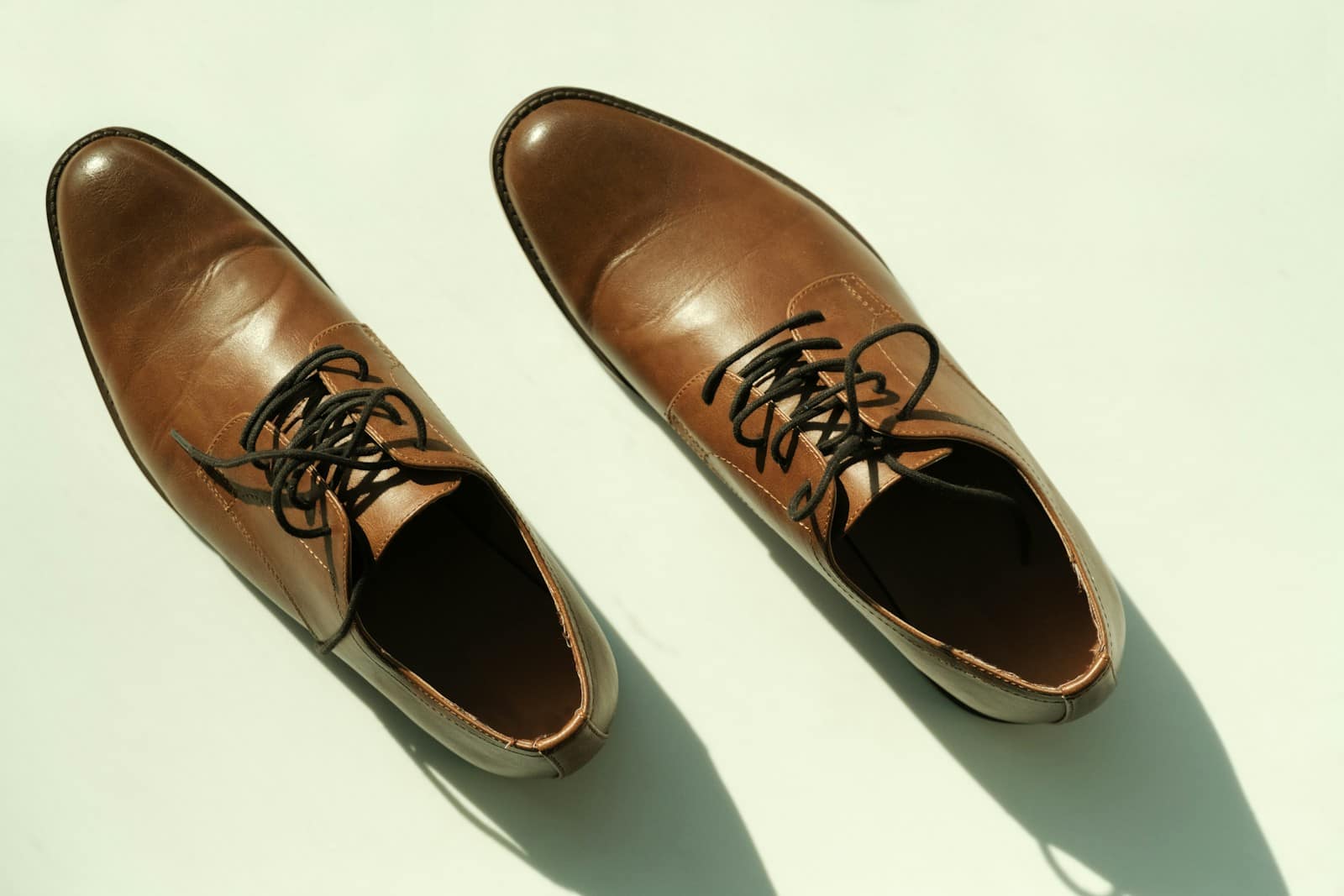 A pair of brown leather lace-up shoes seen from above on a pale floor, laces loose