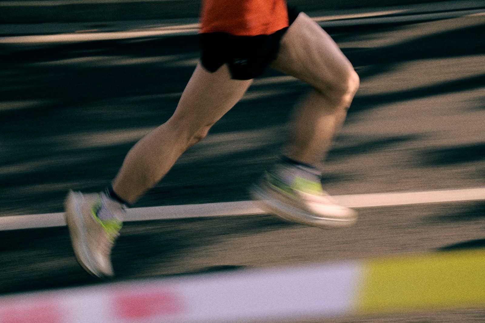 A runner mid-stride on a track, legs and shoes streaked by motion blur against the lane markings