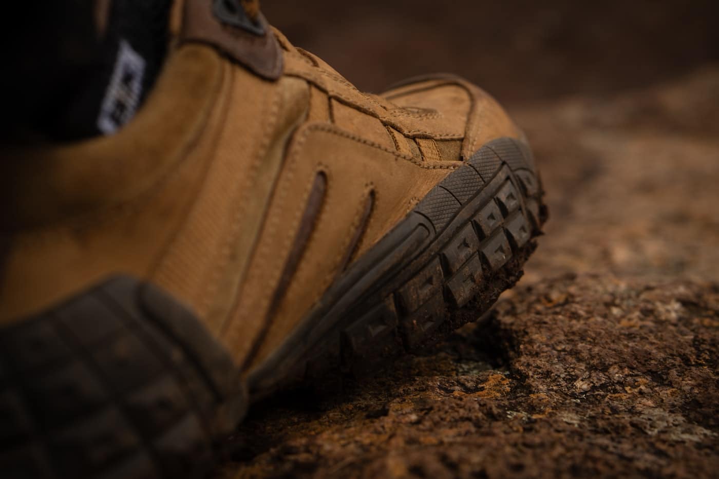 Lugged rubber outsole on a work boot, pressed into dry ground