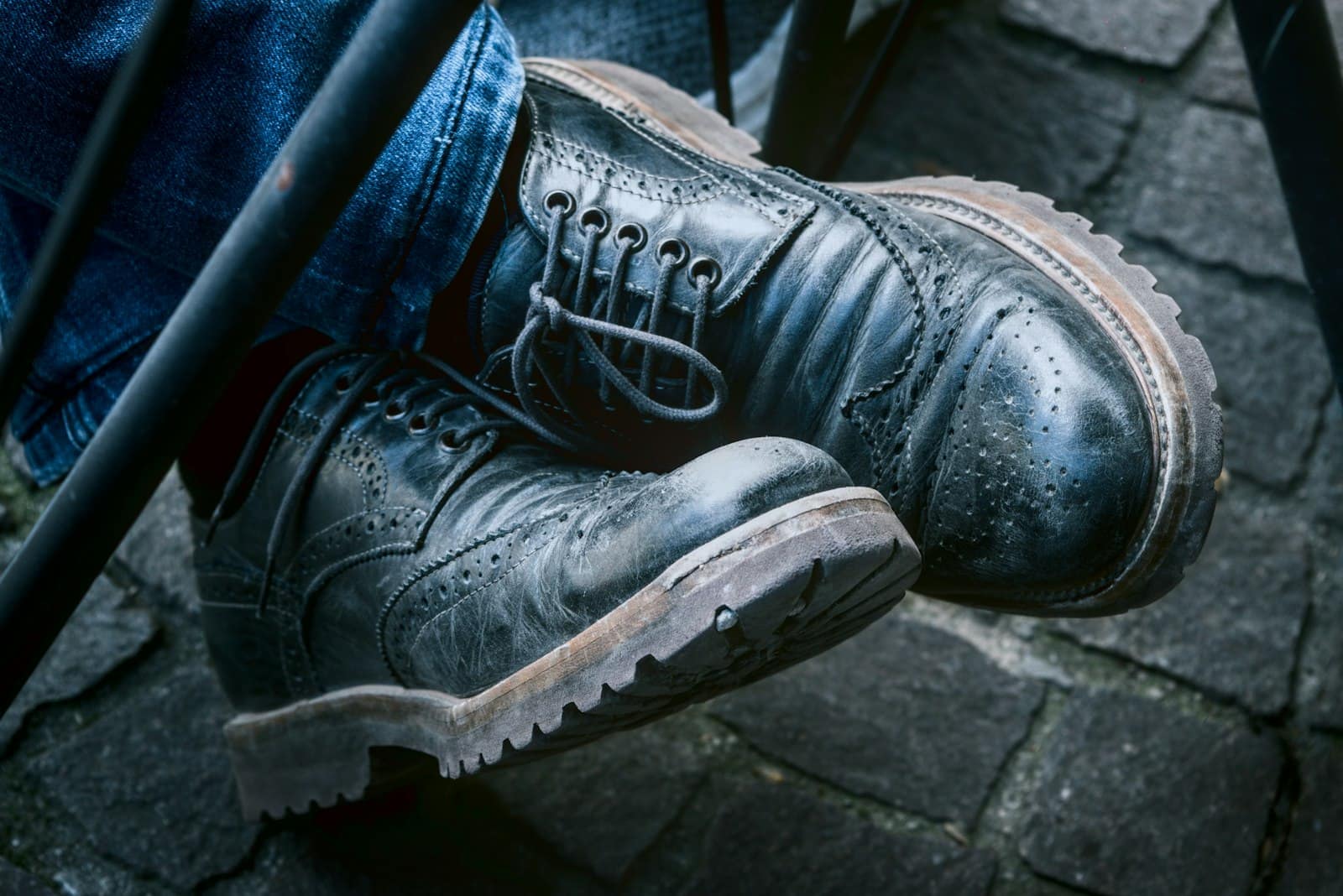 Worn leather brogue boots crossed on stone steps, the lugged rubber outsole edges catching the light