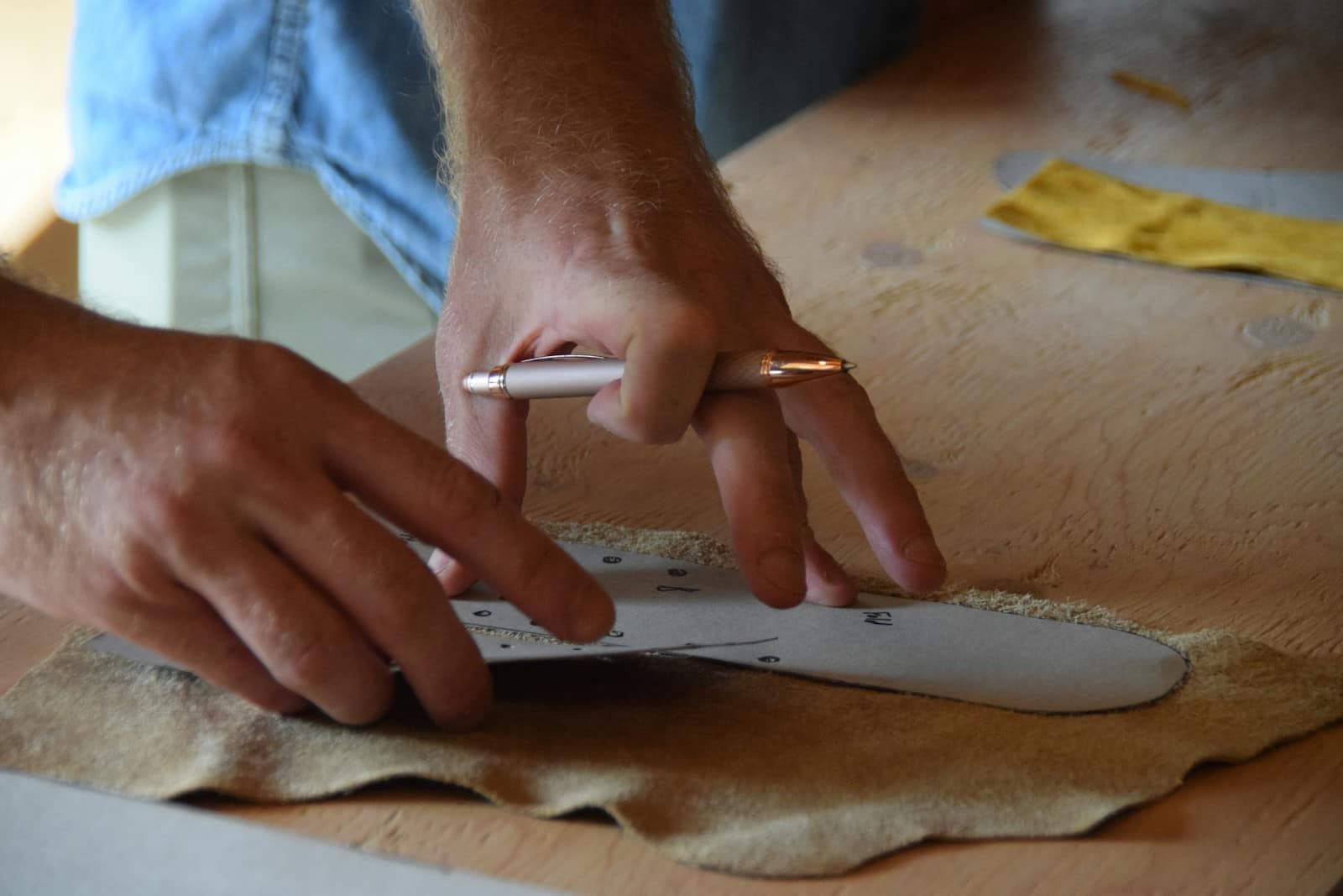 Hands tracing round a paper sole pattern with a pen on a sheet of suede at a workbench