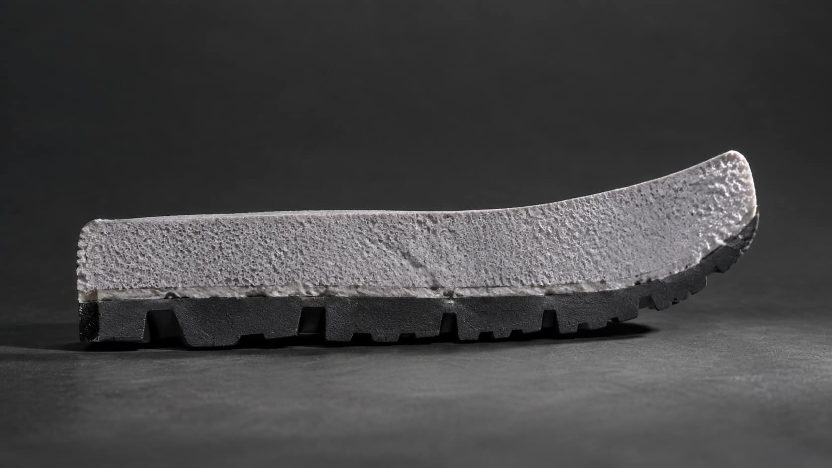A sole cut through on edge: dark rubber outsole below, pale foamed midsole above, the bond line a fine seam between them